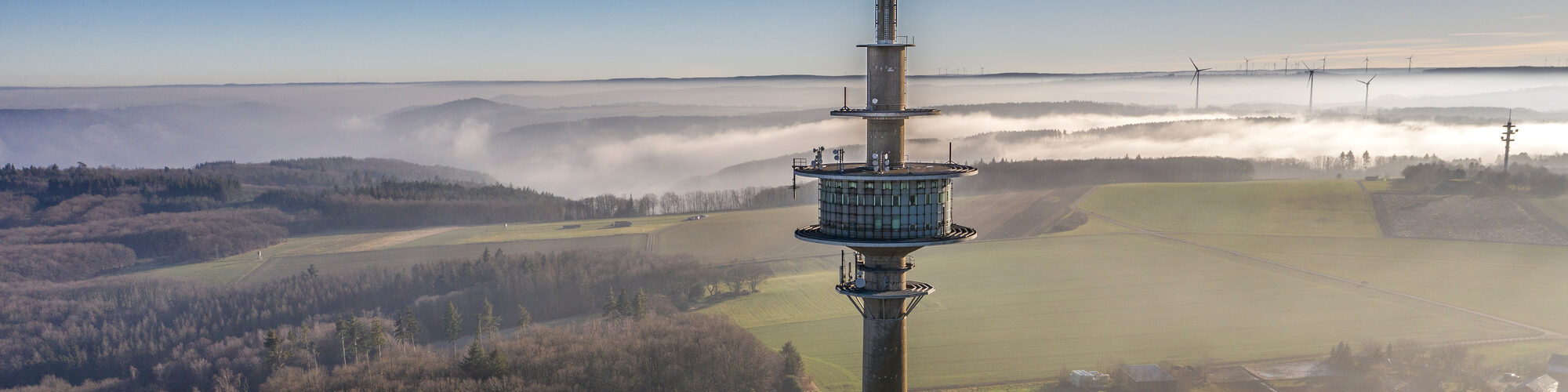 Fernmeldeturm in Großhau in nebligen Morgenstunden, Drohnenaufnahme, im Hintergrund Windkraftanlagen